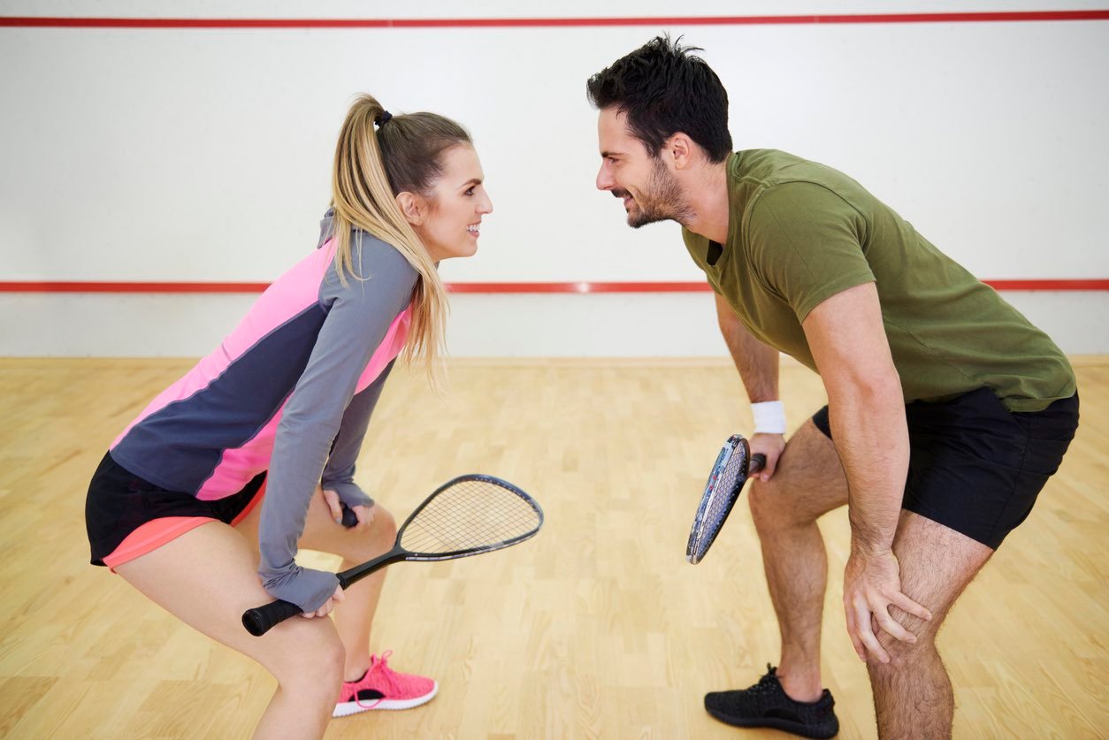 A man and a woman about to play a game of squash. Both are smiling.